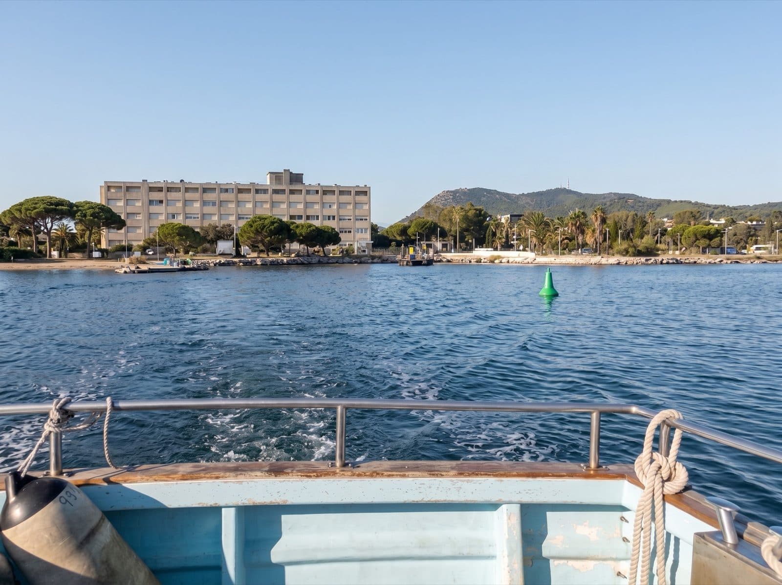 Le bateau-bus s'éloigne des Sablettes, sa poupe et son sillage devant le front de mer et les collines du Var